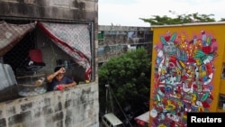 A drone view shows a boy watching outside his apartment next to a mural titled 