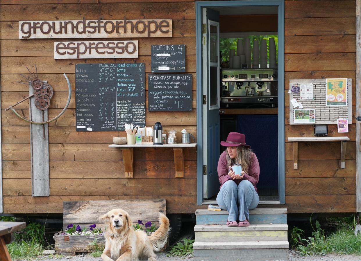 Barista Rose Saturday, 43, drinks coffee on the steps of the Grounds for Hope espresso cabin in Hope, Alaska, while her dog Jack watches for customers.