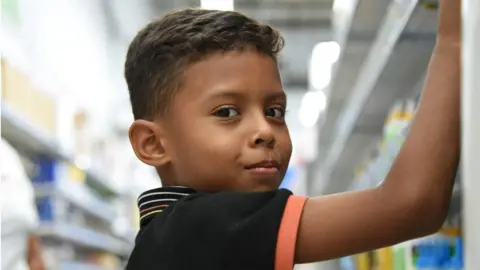 Ed Prior/NRC Eight-year-old Derek is buying pens and books with his mother in a shop in San Pedro Sula, as he prepares to restart following a period where he was not able to attend school