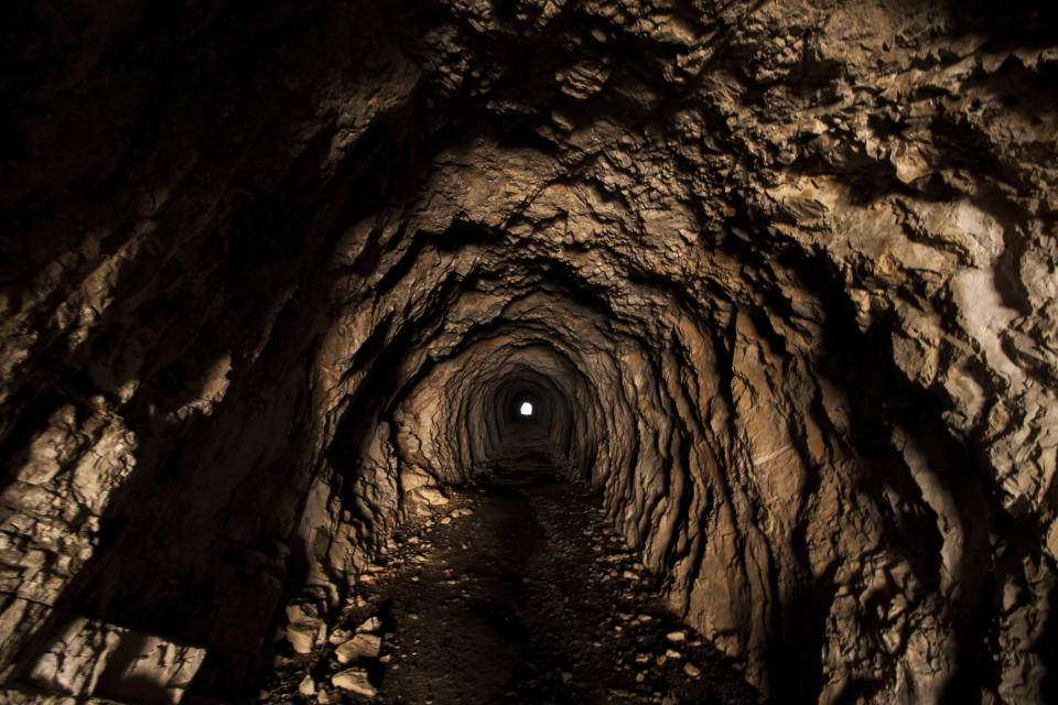 A view of a dark, rocky tunnel with a small circular light source visible at the far end.