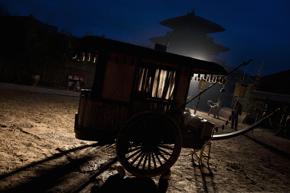 A historical scene with a vintage wooden cart and traditional architecture in the background at dusk.