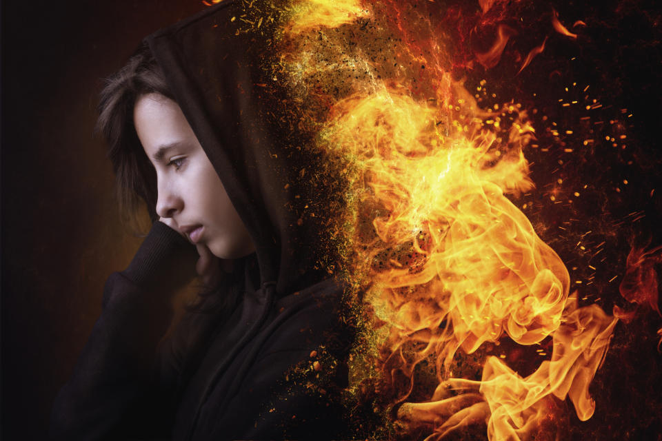 A person in a hooded garment with their side profile in focus. The image artistically transitions from the person's head to flames