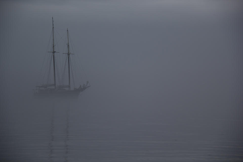 A faint image of a sailboat partially obscured by thick fog on calm waters