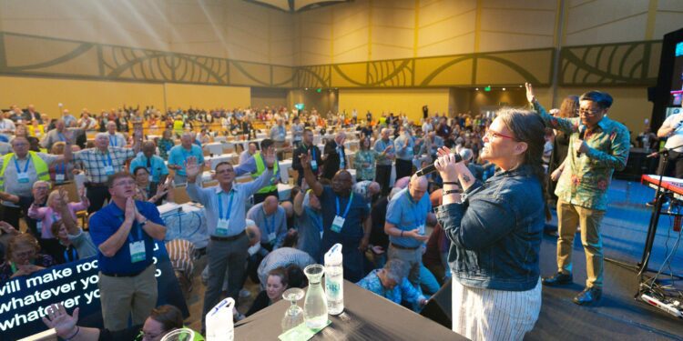 Worshipers in a conference meeting room sing and pray.