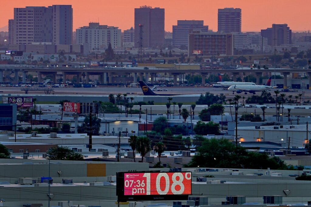 FILE - A sign displays an unofficial temperature as jets taxi at Sky Harbor International Airport at dusk, July 12, 2023, in Phoenix.  Arizona voters are looking to the climate plans of Kamala Harris and Donald Trump amid rising temperatures and other climate change impacts.(AP Photo/Matt York, File)