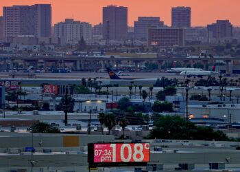 FILE - A sign displays an unofficial temperature as jets taxi at Sky Harbor International Airport at dusk, July 12, 2023, in Phoenix. Arizona voters are looking to the climate plans of Kamala Harris and Donald Trump amid rising temperatures and other climate change impacts.(AP Photo/Matt York, File)