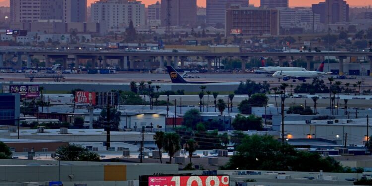 FILE - A sign displays an unofficial temperature as jets taxi at Sky Harbor International Airport at dusk, July 12, 2023, in Phoenix.  Arizona voters are looking to the climate plans of Kamala Harris and Donald Trump amid rising temperatures and other climate change impacts.(AP Photo/Matt York, File)