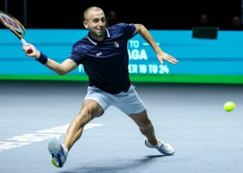 Dan Evans lunges for a forehand in the Davis Cup 2024, wearing a blue shirt and white shorts.
