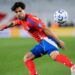 Victor Davila flicks the ball on the pitch, in his red shirt and blue shorts, ahead of the Chile vs Bolivia live stream.