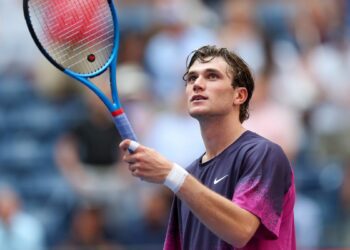 Jack Draper raises his racket at the US Open tennis, wearing a purple Nike t-shirt.