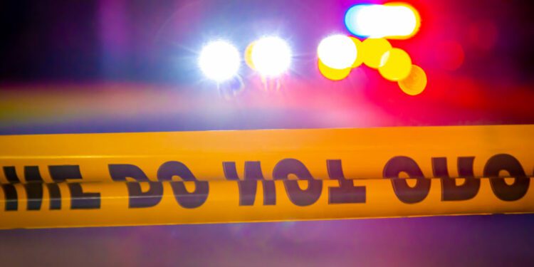 Generic and blurry police lights from a cruiser vehicle and car headlights behind yellow crime scene do not cross caution ...