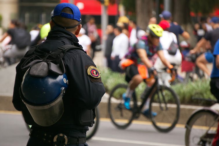 A Mexican policeman watches people walk and cycle down a street in Mexico City.