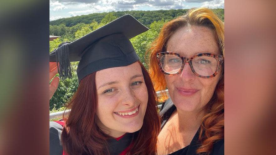 Daisy Cadet and her mother Ashleigh smiling. Daisy is wearing a graduation gown and hat, she has red hair. Her mum Ashleigh is also smiling at the camera, she has ginger hair and is wearing a black top. 