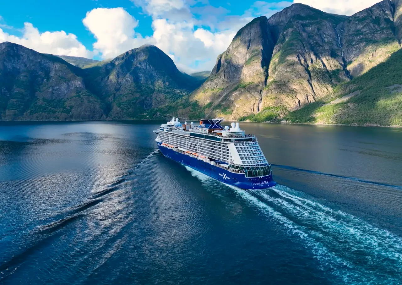 Celebrity Cruises ship sailing through a scenic fjord in Norway surrounded by towering mountains.