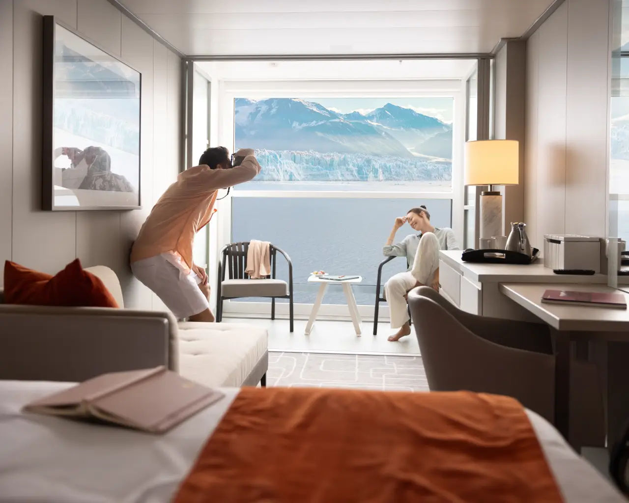 A couple enjoying the view of Alaskan mountains and glaciers from a stateroom on a Celebrity Cruises ship.