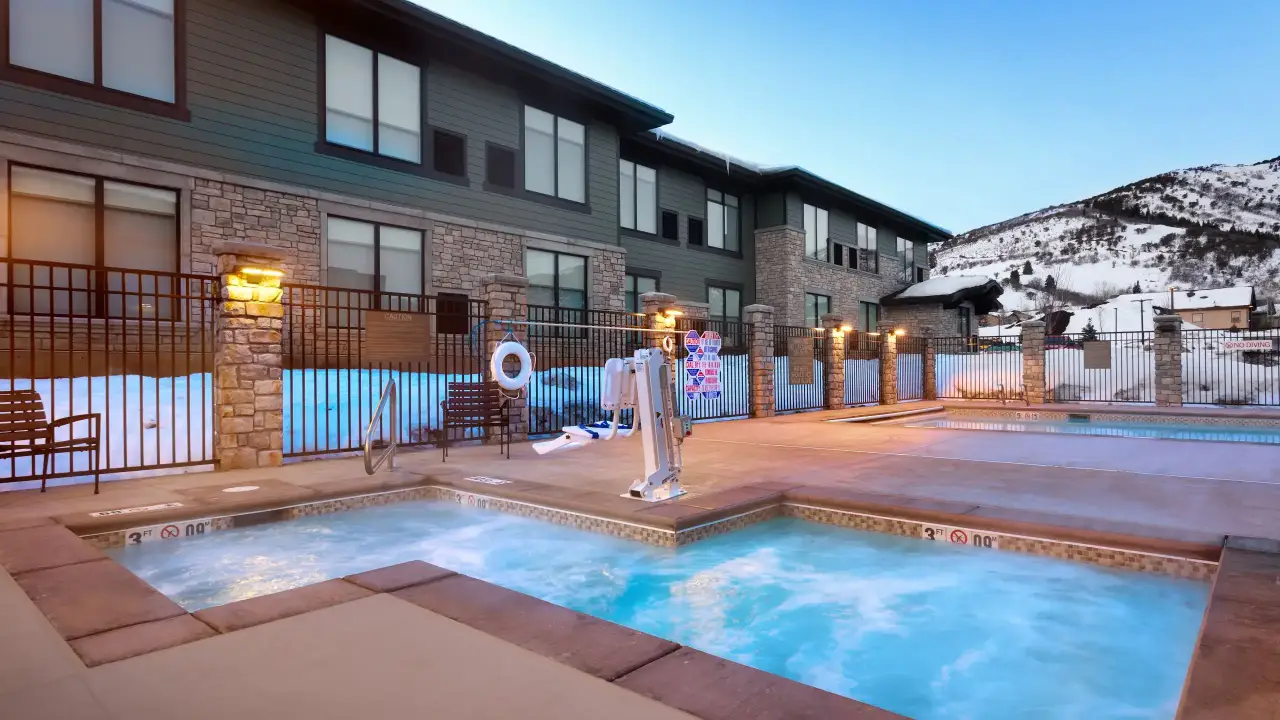 Outdoor jetted tub and swimming pool at one of the best mountain resorts for family ski trips: Hyatt Place Park City with snow-covered mountains in the background.