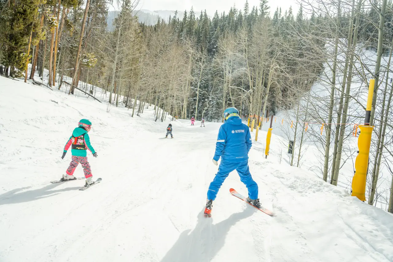 Ski instructor guiding children down a snowy slope at Keystone Resort, a popular mountain resort for family ski trips.