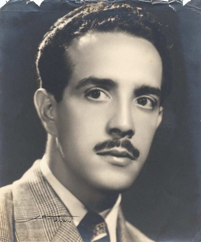 Rafael Soriano as a 27-year-old in Cuba. It is a black and white headshot of a young man with dark wavy hair and a mustache wearing a suit and tie, with a dark background. 