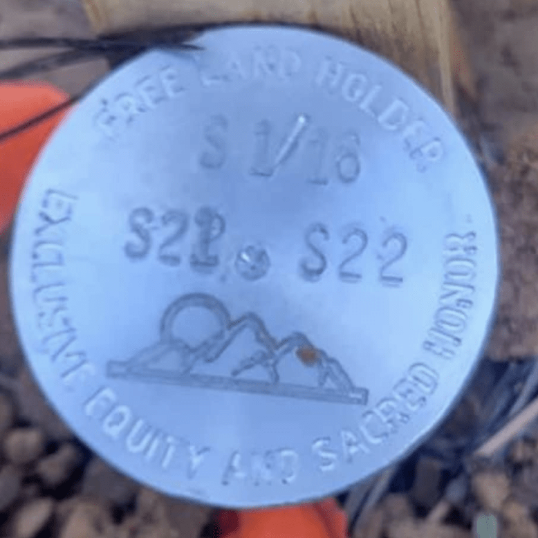 A silver metal medallion at the base of a wooden post that reads 