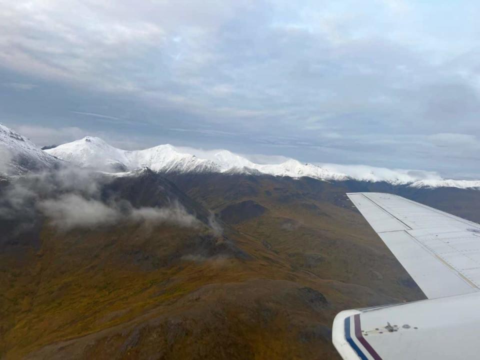 A plane flies over snowy mountain peaks in Gates of the Arctic National Park