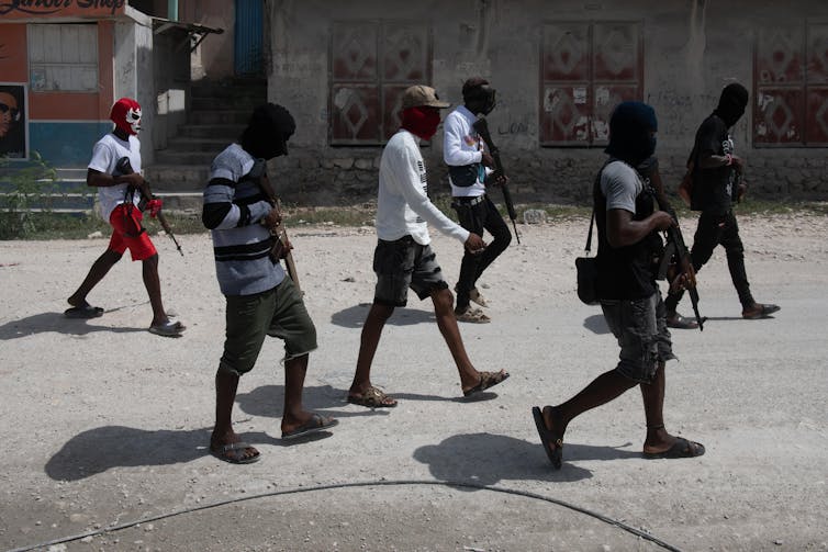 Six masked armed gang members walk down a street in Haiti.