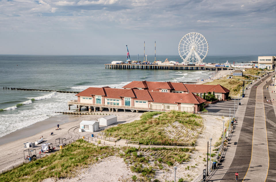 Beach scene with a boardwalk, ocean waves, a pier featuring a Ferris wheel, and sand dunes in the foreground