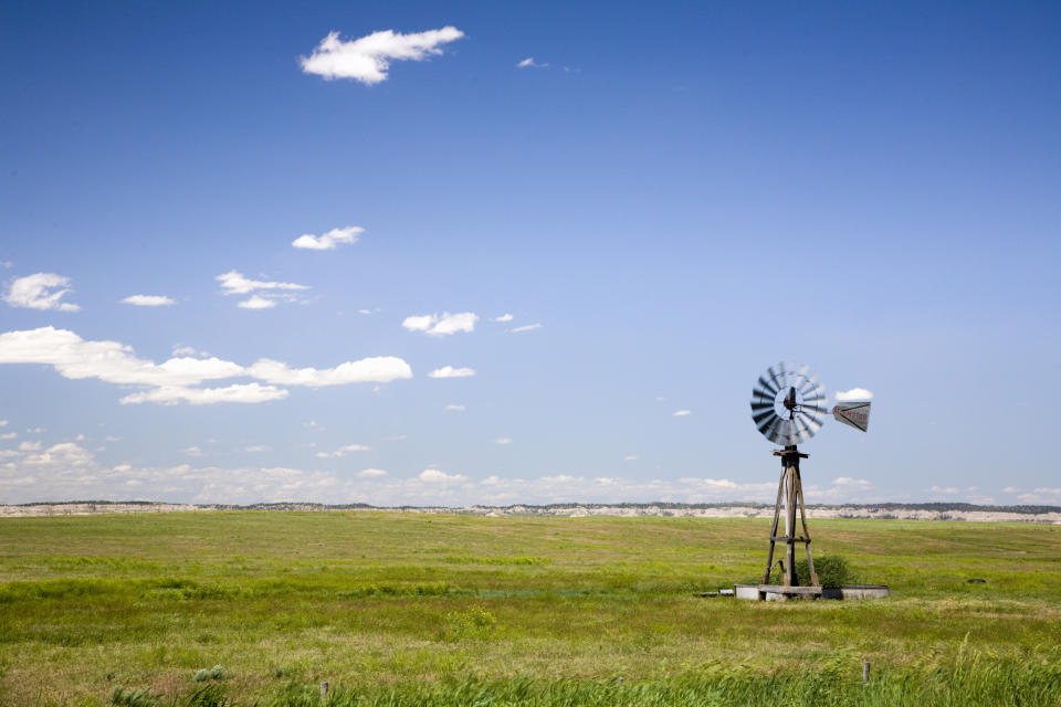 A solitary windmill stands in a vast grassy field under a clear sky