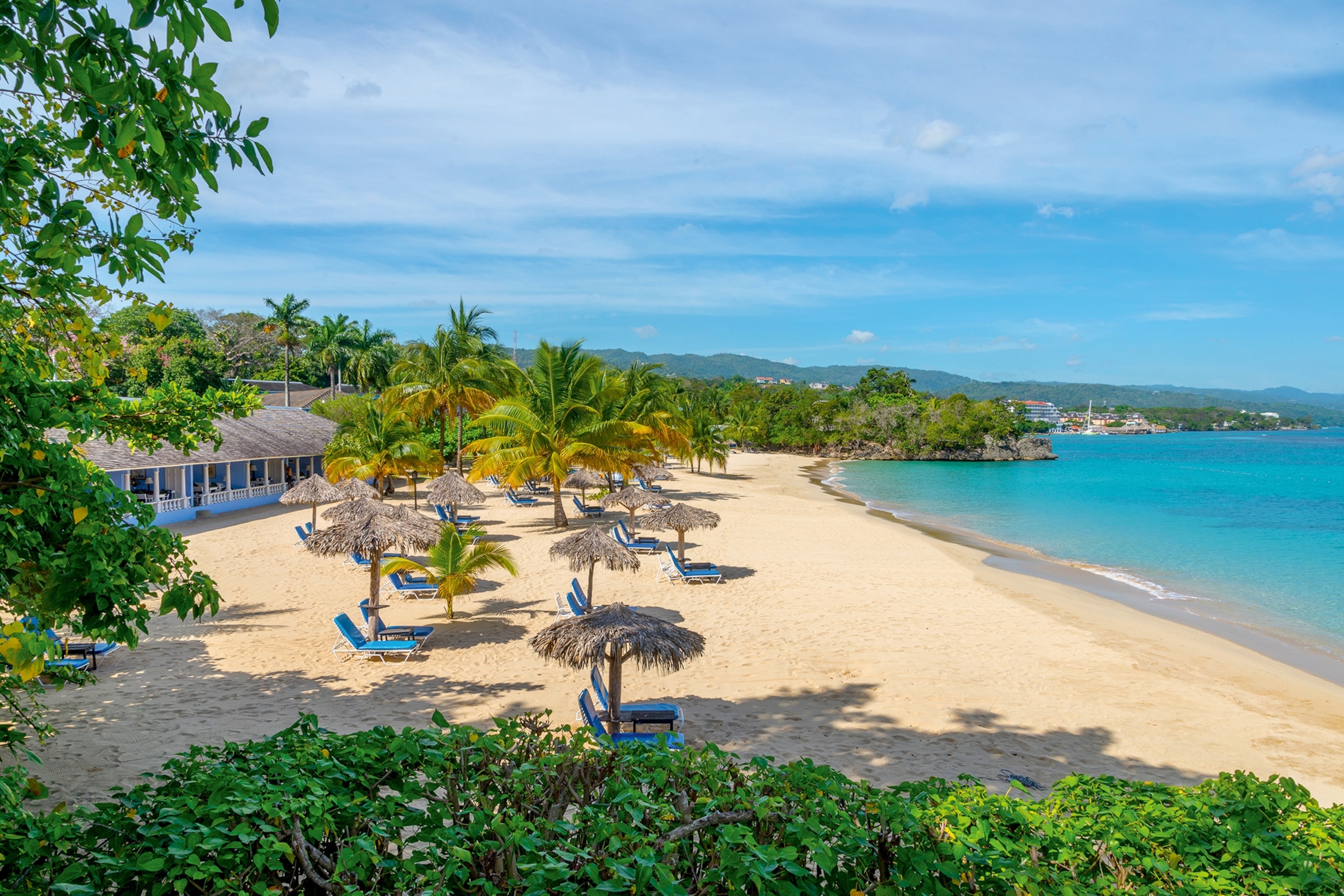 Golden sandy beach with turquoise waters, palm trees and sun loungers on the shore