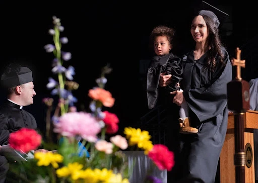 Katie Chihoski, the first mom to graduate from University of Mary’s St. Teresa of Calcutta Community for Mothers, walks across the stage with her daughter Lucia. Credit: Mike McCleary/University of Mary