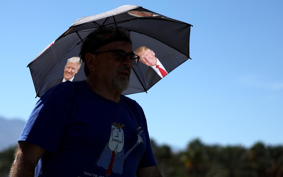 A supporter stands under an umbrella with images of Donald Trump.