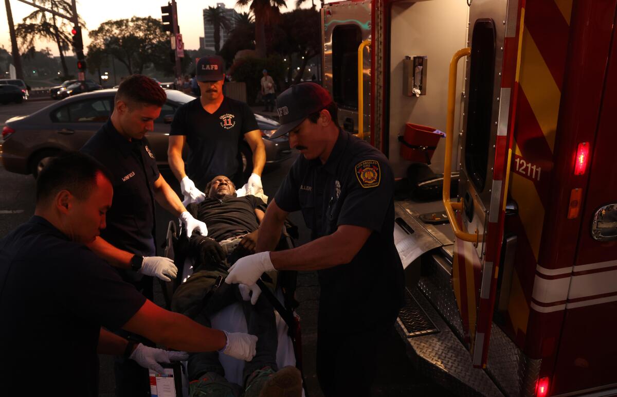 A man lays on a gurney surrounded by EMTs and firefighters.