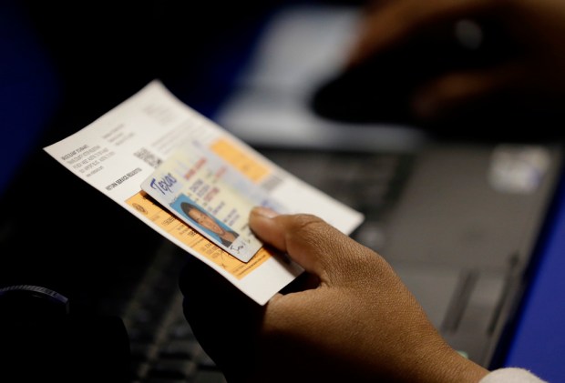 FILE – An election official checks a voter’s photo identification...