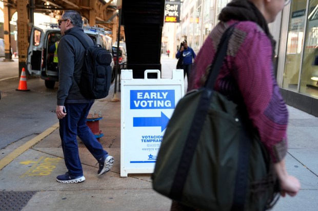 FILE – People walk by an early voting sign on...