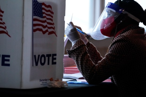 FILE – A poll worker talks to a voter before...