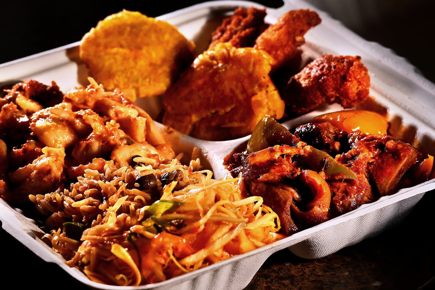 Haitian mac and cheese, made with ground turkey and epis (far left); pwa congo, black pigeon beans and rice; and pikliz (foreground) share a platter with sos cabrit (goat stew, at right). In the background are fried plantains and akra, root vegetable fritters. 