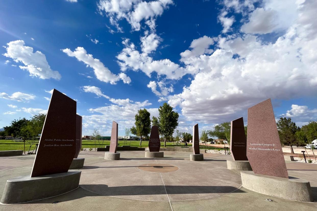 A group of reddish flat slabs on round bases at a park under blue skies and clouds