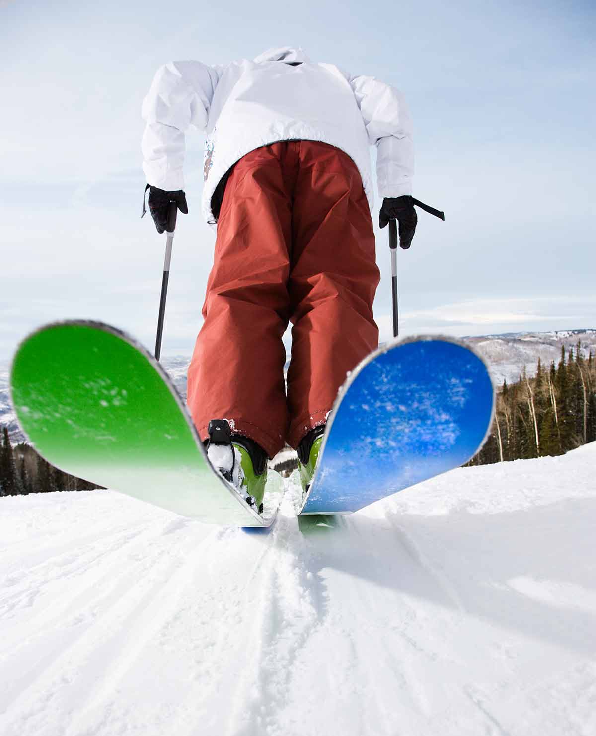 back view of man leaning on his skis getting ready to ski down a mountain