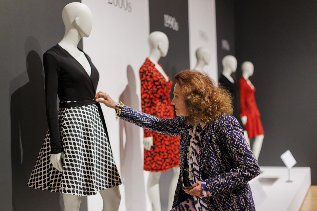 Diane von Furstenberg looks at a black-and-white dress; a bright red dress is next to it. 