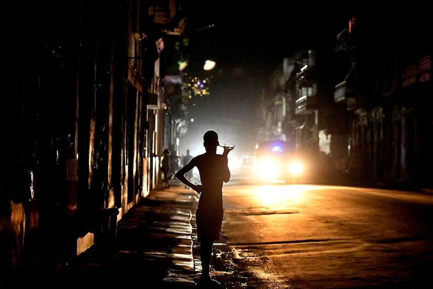 A silhoutte of a person standing on a street in a blackout. 