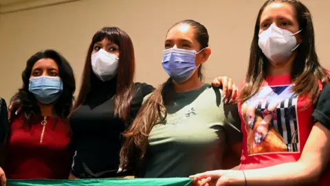 Getty Images Four Salvadoran women stand together holding a large green handkerchief