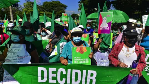 Getty Images Women holding green umbrellas and signs at a protest in San Salvador, September 2021