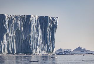 A massive iceberg stands above the calm water in the Ilulissat Icefjord in Greenland