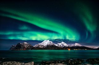 The green northern lights light up the night sky in Greenland above snow-covered mountains