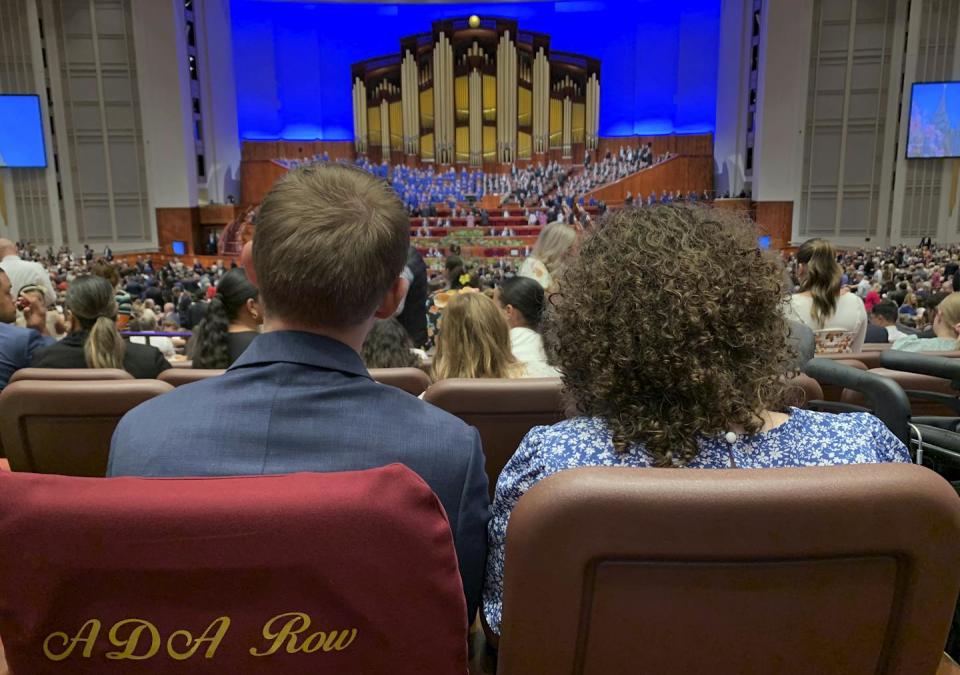 A man and a woman, seated with their backs to the camera, look toward a large organ on stage in an auditorium.