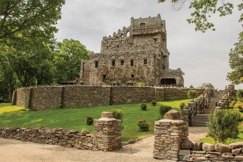 Stone castle with towers and crenellations, surrounded by grass and trees, with a stone path and staircase leading up.