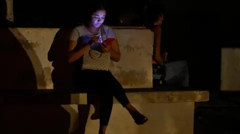 AFP A woman is lit by her mobile phone during the third night of a nationwide blackout in Havana October 20, 2024. 