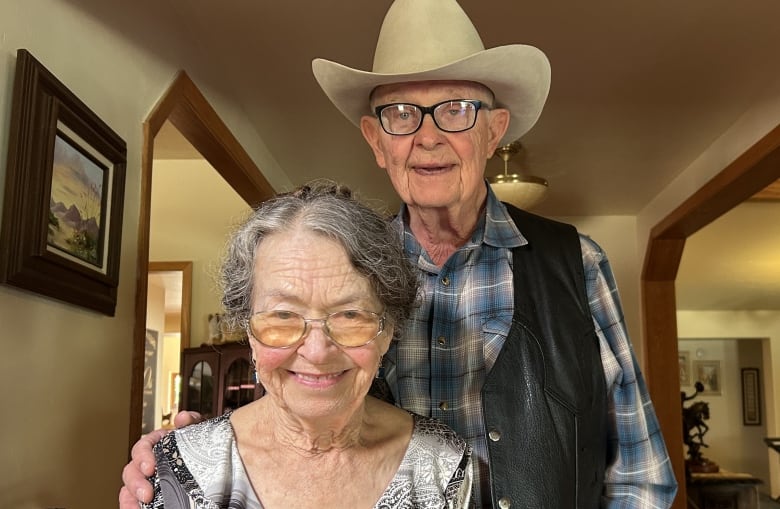 A man and woman stand in their house, smiling for the camera. 