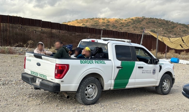 People sit in the back of a vehicle in the desert. The side of the vehicle says Border Patrol.