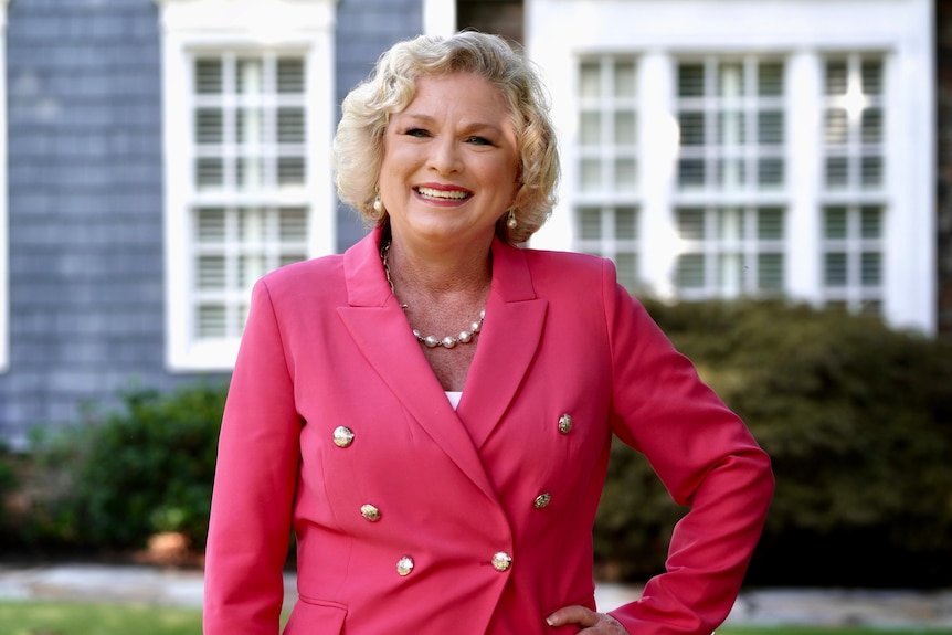 A woman in a hot pink, double breasted suit jacket poses with her hand on her hip