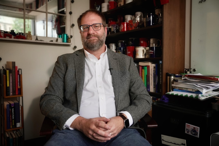 a man sits on an office chair in a messy office